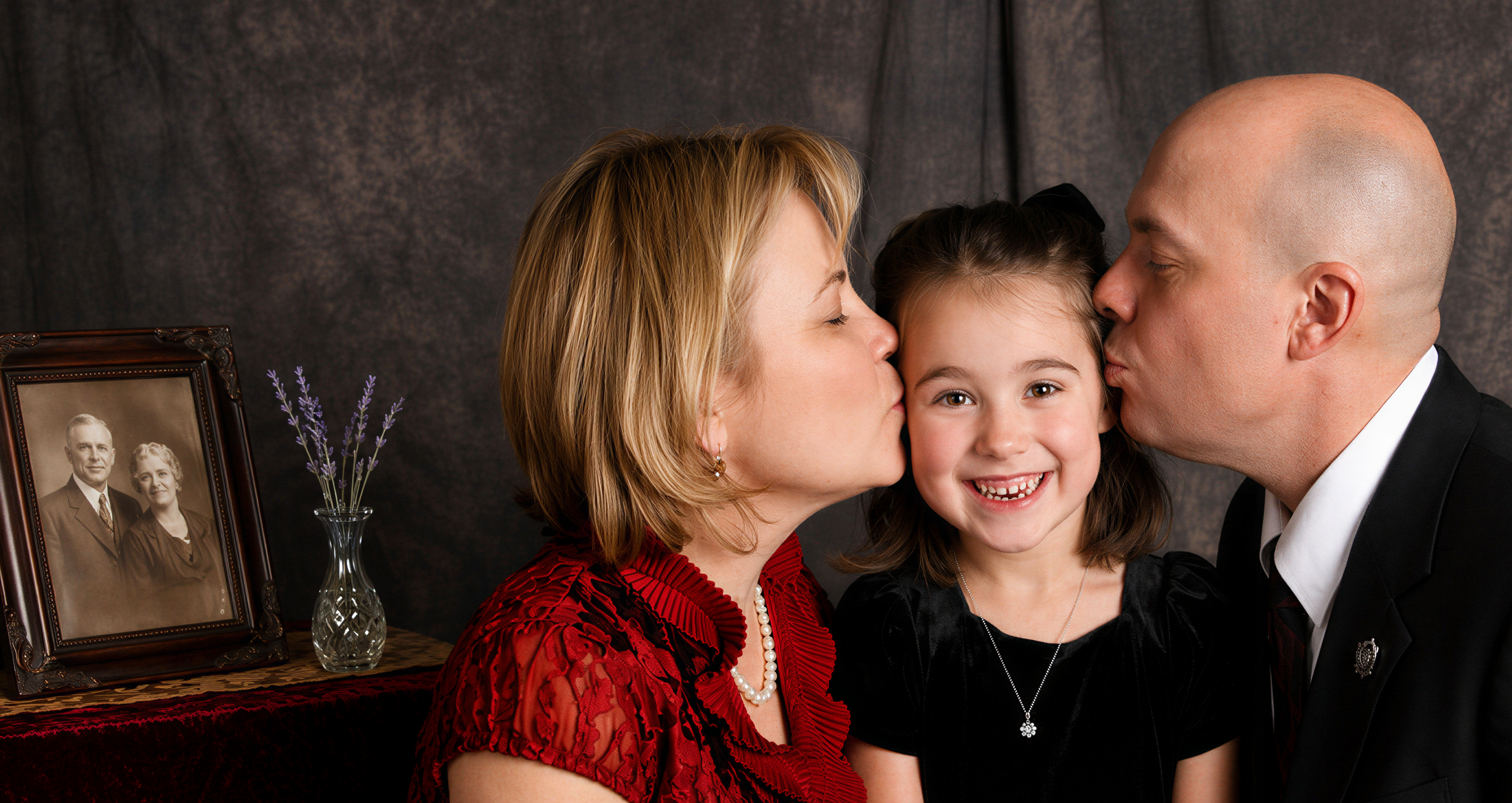 A mother and father kissing their smiling daughter