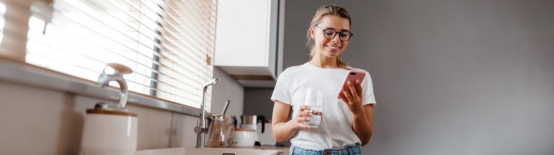 Woman with a glass of water checking her phone in the kitchen